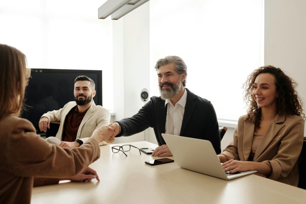 A group of business professionals shake hands during a meeting in a modern office setting.
