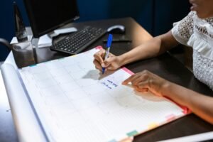 Person writing important notes in a desk calendar with a pen, set in an office.